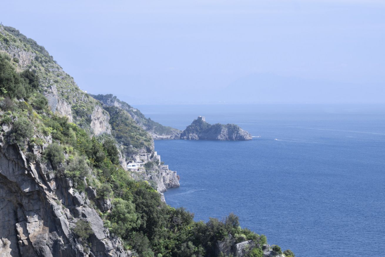 Un paysage côtier avec une falaise rocheuse, un petit bâtiment situé sur la falaise et une île au loin.