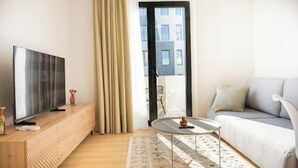 En moderne stue med et fladskærms-tv på et træpanel, et rundt sofabord, en sofa og en gulvtæppe med mønster.