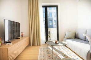 Ein modernes Wohnzimmer mit Flachbildfernseher auf einer Holzkonsole, einem runden Couchtisch, einer Couch und einem gemusterten Teppich.
