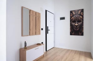 Ein Zimmer mit Holzboden, weißer Wand, Holzschrank, Spiegel, Tür und einem gerahmten Kunstwerk.