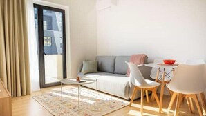 En moderne stue med sofa, spisebord med stole, sofabord og et stort vindue med gardiner.
