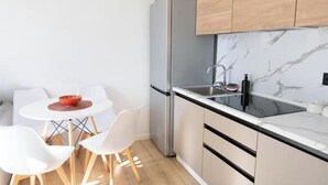 Et kompakt køkken med et moderne design, der inkluderer et stålkøleskab, en sort bordplade og træskabe.