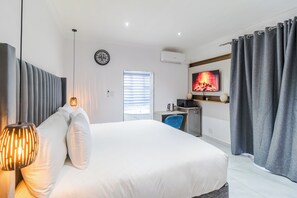 Ein modernes Hotelzimmer mit einem großen Bett, einem Schreibtisch, einem Fernseher und einem Fenster mit Jalousien.