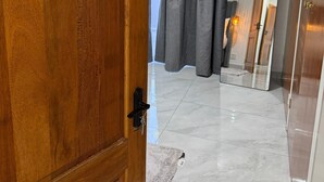 Una puerta de madera, una cortina gris, un suelo de baldosas y un espejo.