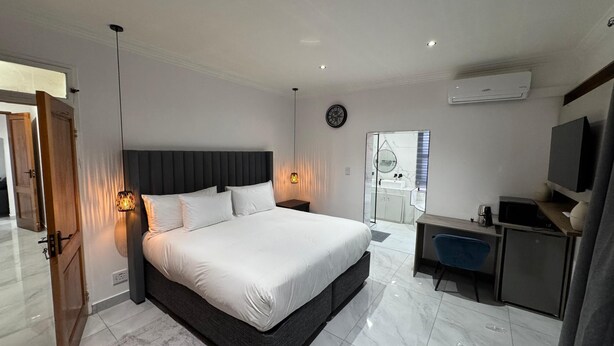 Un dormitorio moderno con una cama grande, lámparas de noche, televisión y un baño visible a través de una puerta de cristal.