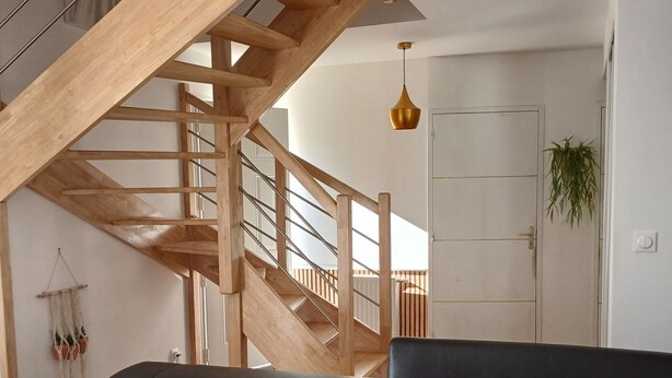 Un salon moderne avec un canapé en cuir noir, un escalier en bois et une suspension décorative.