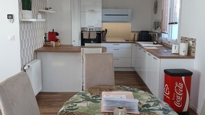 Une cuisine compacte avec des meubles blancs, un coin repas avec une table dressée pour deux personnes et une poubelle rouge.