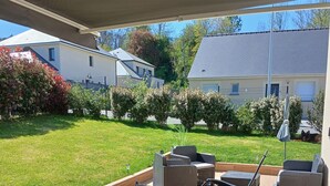 Une terrasse extérieure avec une table et des chaises, entourée d’une clôture et de verdure.