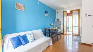 Una habitación con pared azul, un sofá blanco con cojines de diseño azul y blanco, una mesa de comedor con sillas, un microondas y un reloj en la pared.