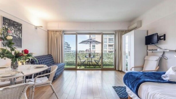 Una habitació d'hotel amb un llit, una taula de dinar amb cadires, un sofà, un balcó amb taula i cadires, i un televisor penjat a la paret.