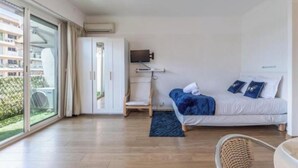 Habitació d'hotel moderna amb un gran finestral corredís que dona a l'exterior, un llit amb roba de llit blava, un televisor de pantalla plana penjat a la paret i un terra de fusta.