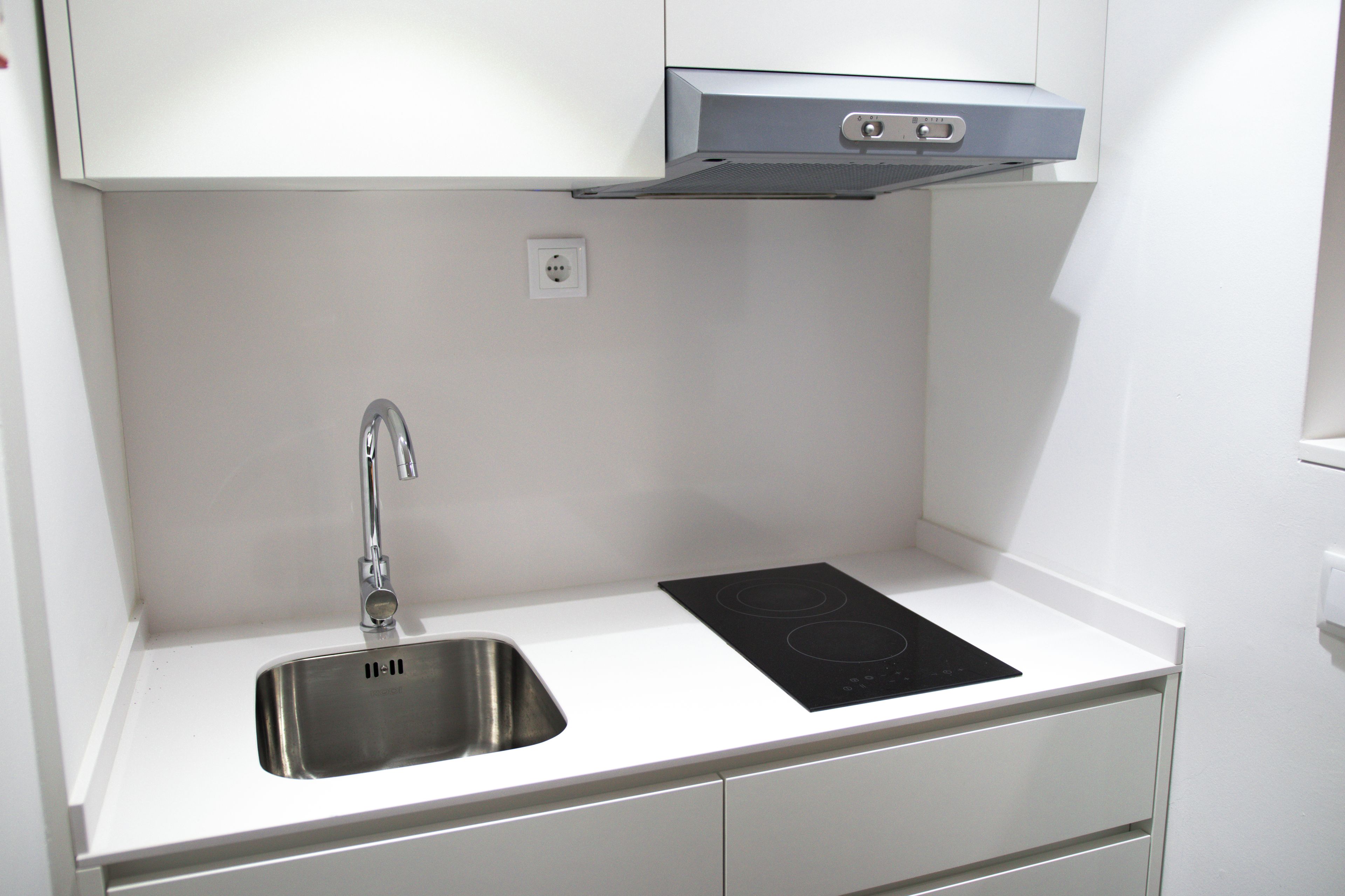 A kitchen with a stainless steel sink, a built-in stovetop, and white cabinetry.