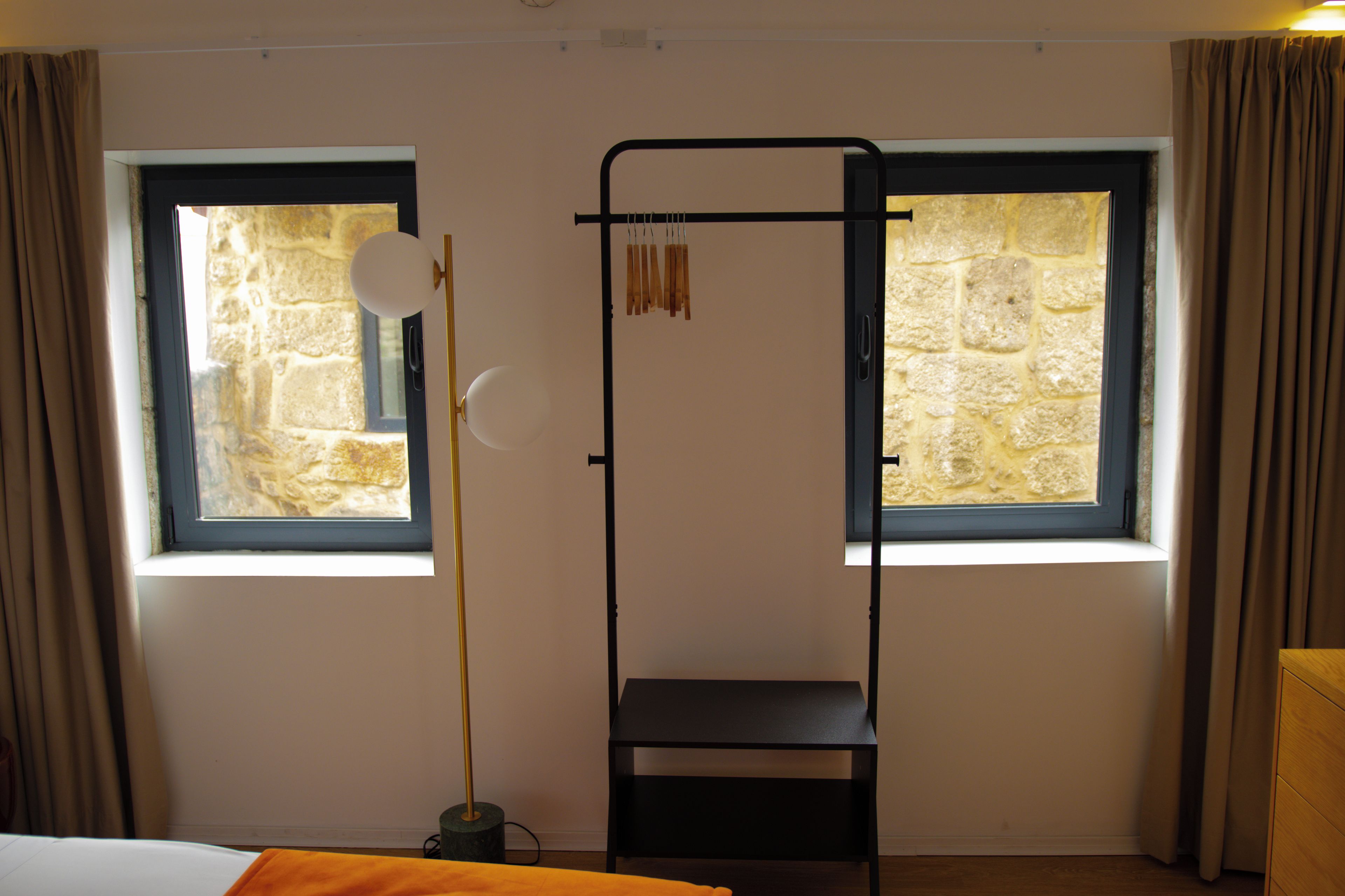 A room with two windows, a black metal stand, a white lamp, and a wooden dresser.