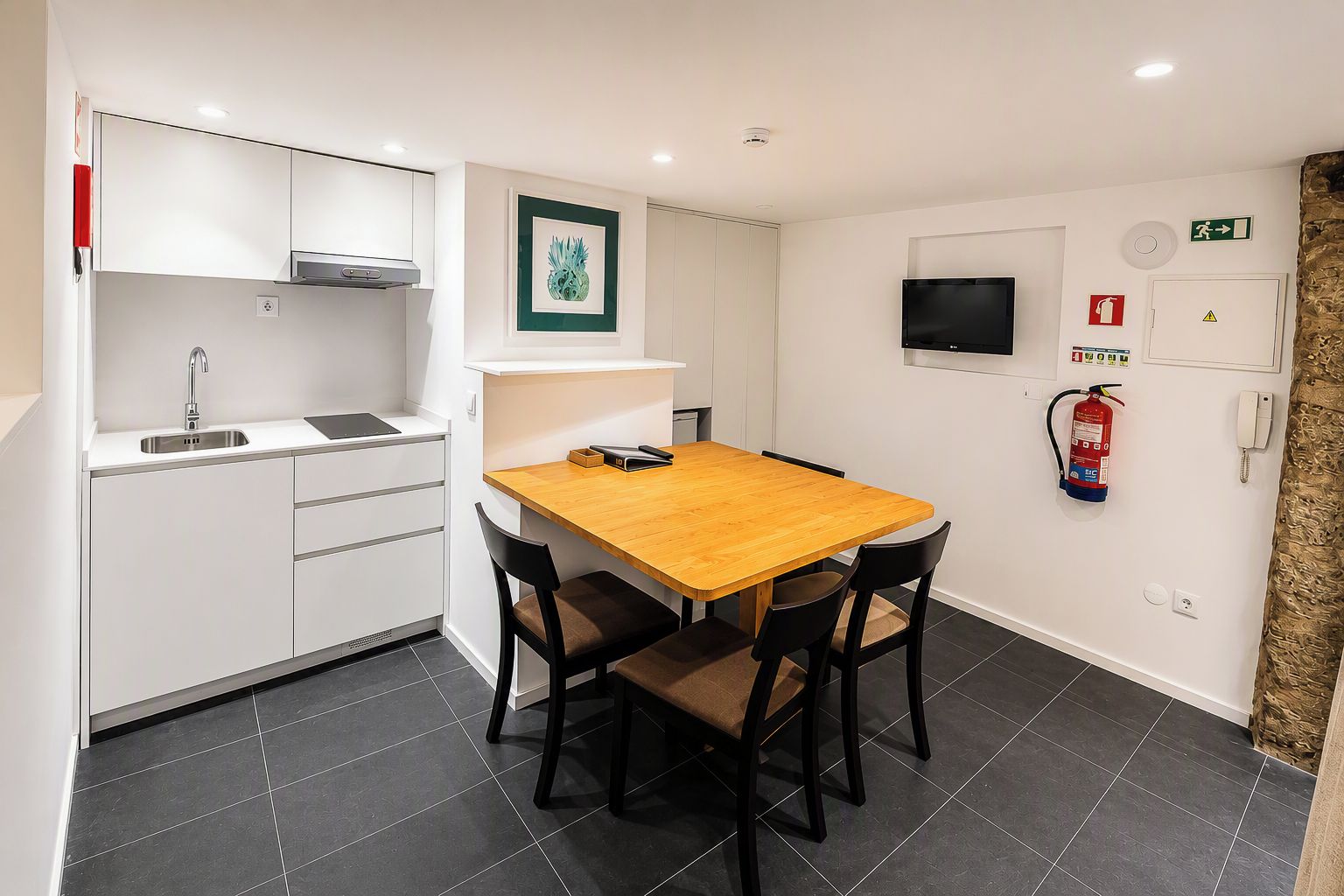 A compact kitchen with a wooden table and chairs, a built-in microwave, and a fire extinguisher on the wall.