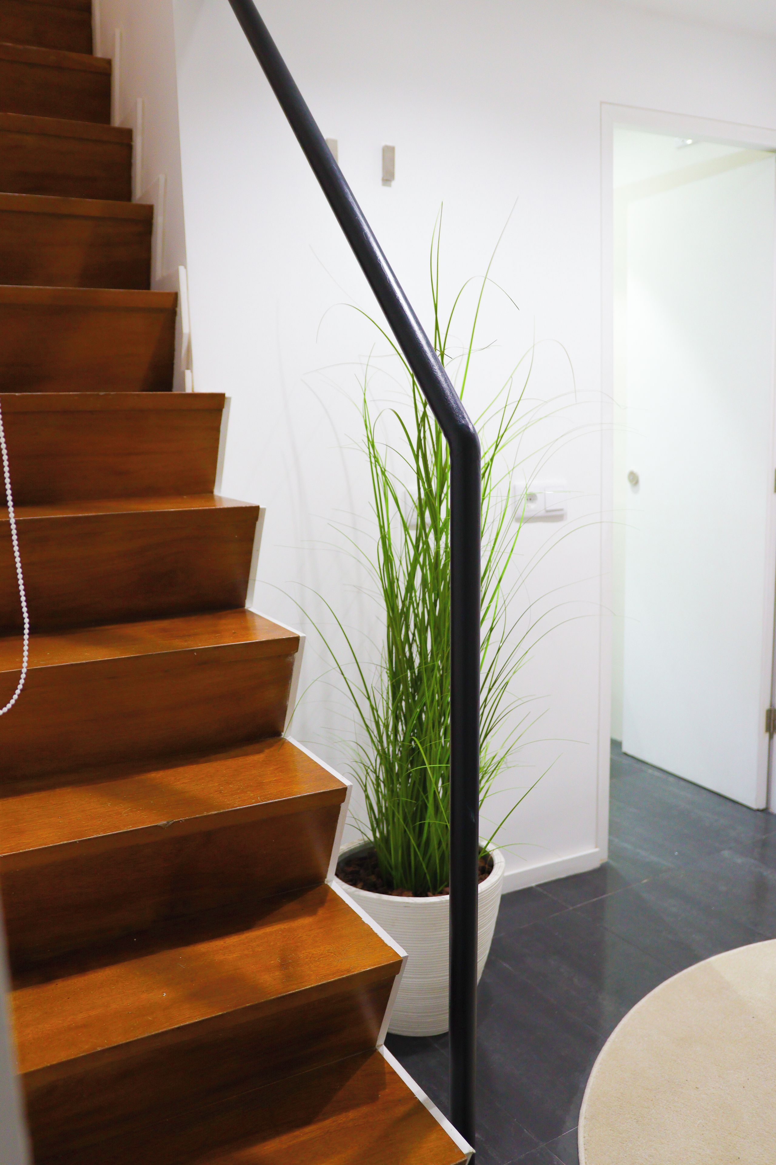 A wooden staircase with a black handrail leading to a white door.