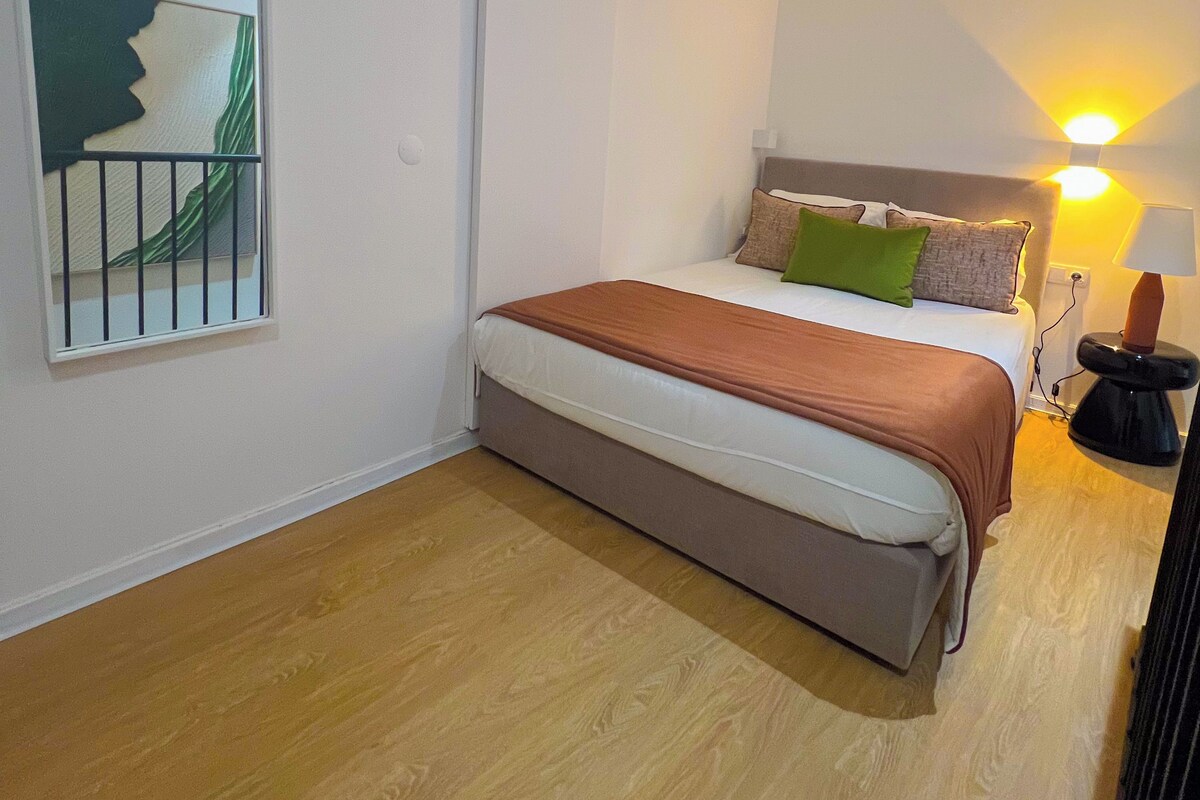 Ein Schlafzimmer mit einem Bett, einem Nachttisch, einer Lampe und einem Fenster mit Blick.