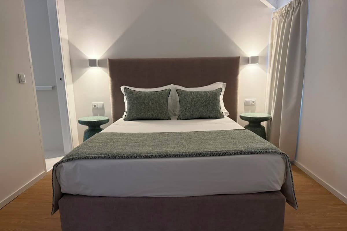 A neatly made bed with a headboard, two bedside tables with lamps, and a green throw blanket.