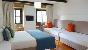 A hotel room with a bed, two sofas, a television, and a window with curtains.