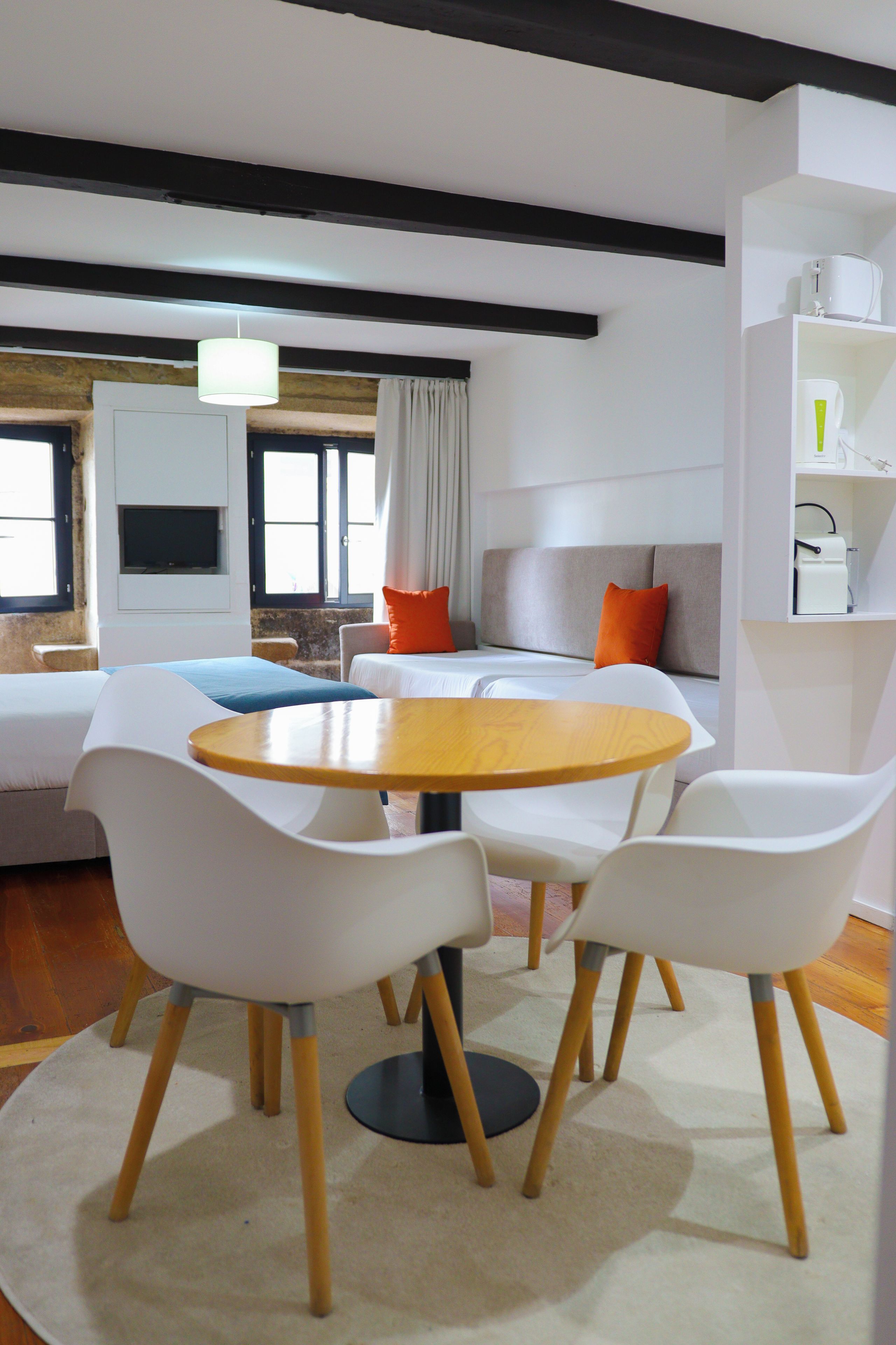 Una sala de estar moderna con una mesa redonda de madera, sillas blancas, un sofá y una televisión.