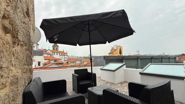 A rooftop terrace with outdoor furniture, a large umbrella, and a view of city buildings. - Oporto Riverside Apartments (Porto)