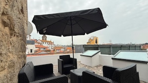 A rooftop terrace with outdoor furniture, a large umbrella, and a view of city buildings. - Oporto Riverside Apartments (Porto)