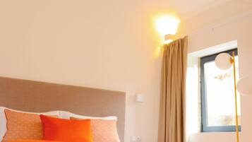 A bedroom with a bed, a nightstand, a lamp, a window with curtains, and a wooden ceiling.
