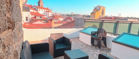 Une terrasse sur le toit, aménagée avec des meubles en osier, une table de billard et offrant une vue sur le paysage urbain, notamment sur une église.