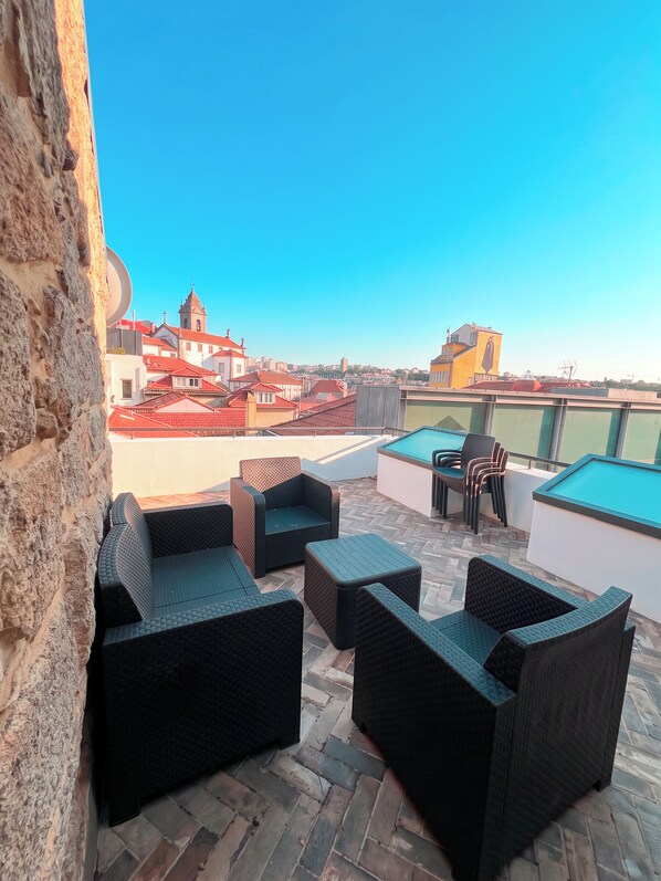 A rooftop terrace with wicker furniture, a pool table, and a view of a cityscape including a church. - Oporto Riverside Apartments (Porto)