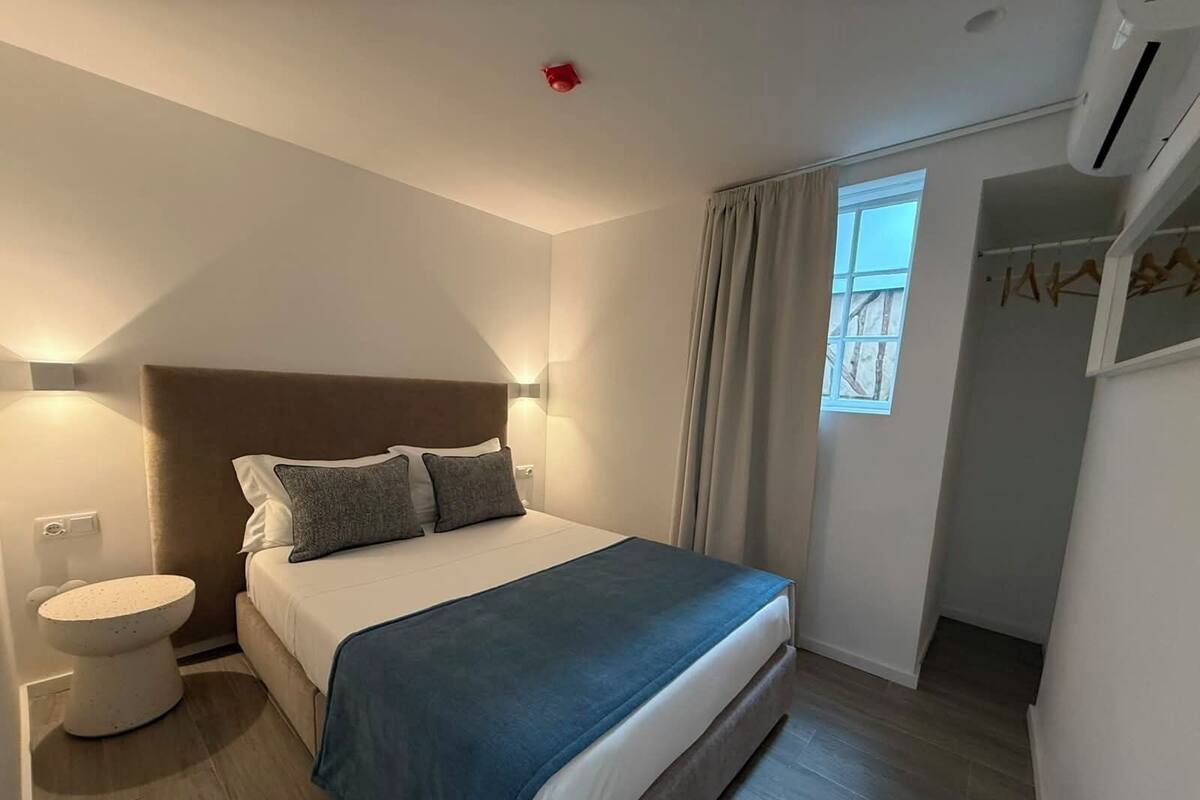 A bedroom with a bed, bedside table, and a window with curtains.