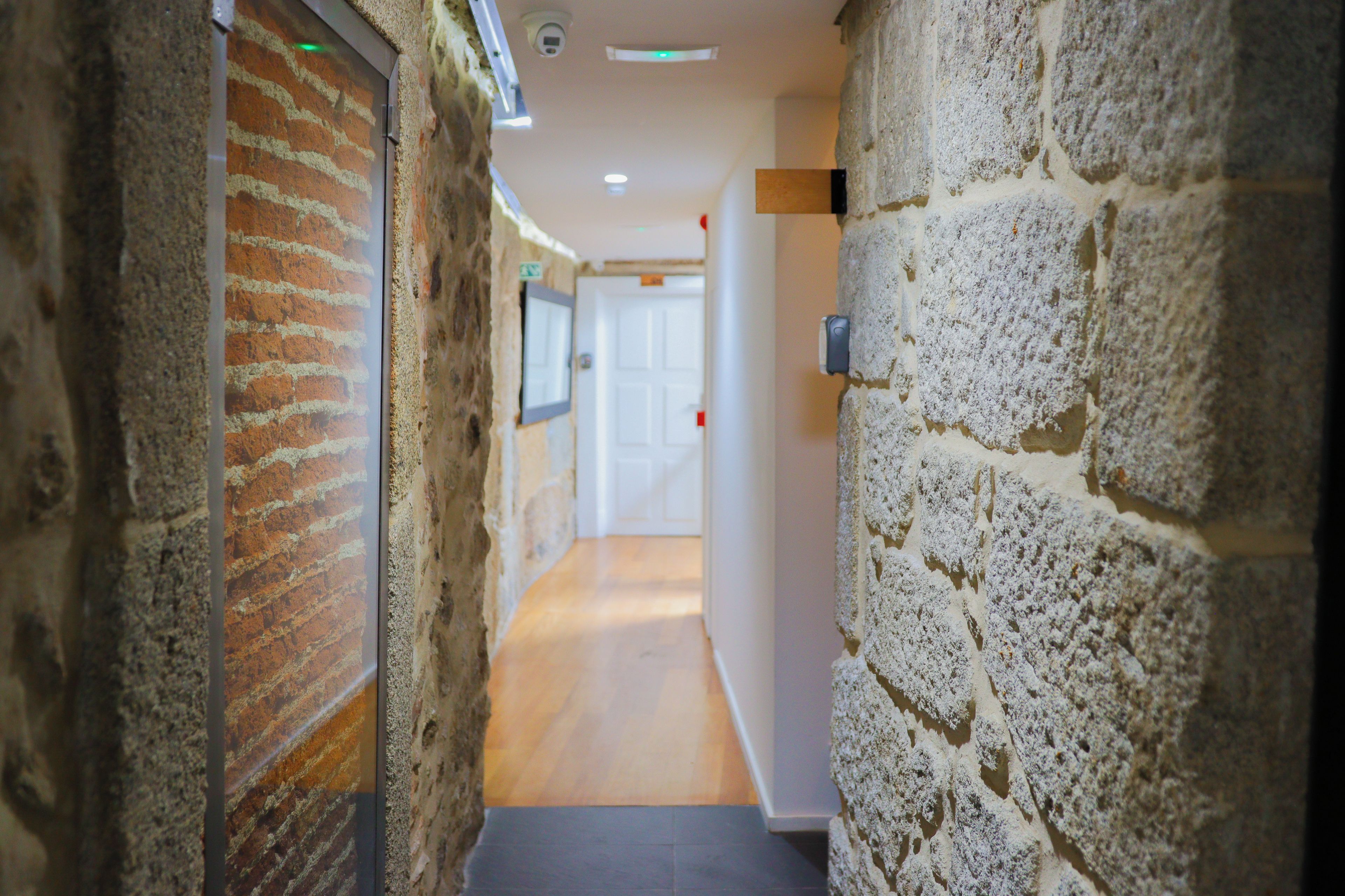 A corridor with stone walls, a wooden floor, and a door at the end.