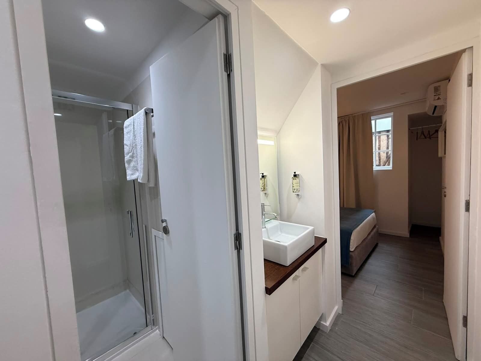 Une chambre d’hôtel équipée d’une douche, d’un lavabo, d’un miroir, d’un lit et d’une fenêtre.