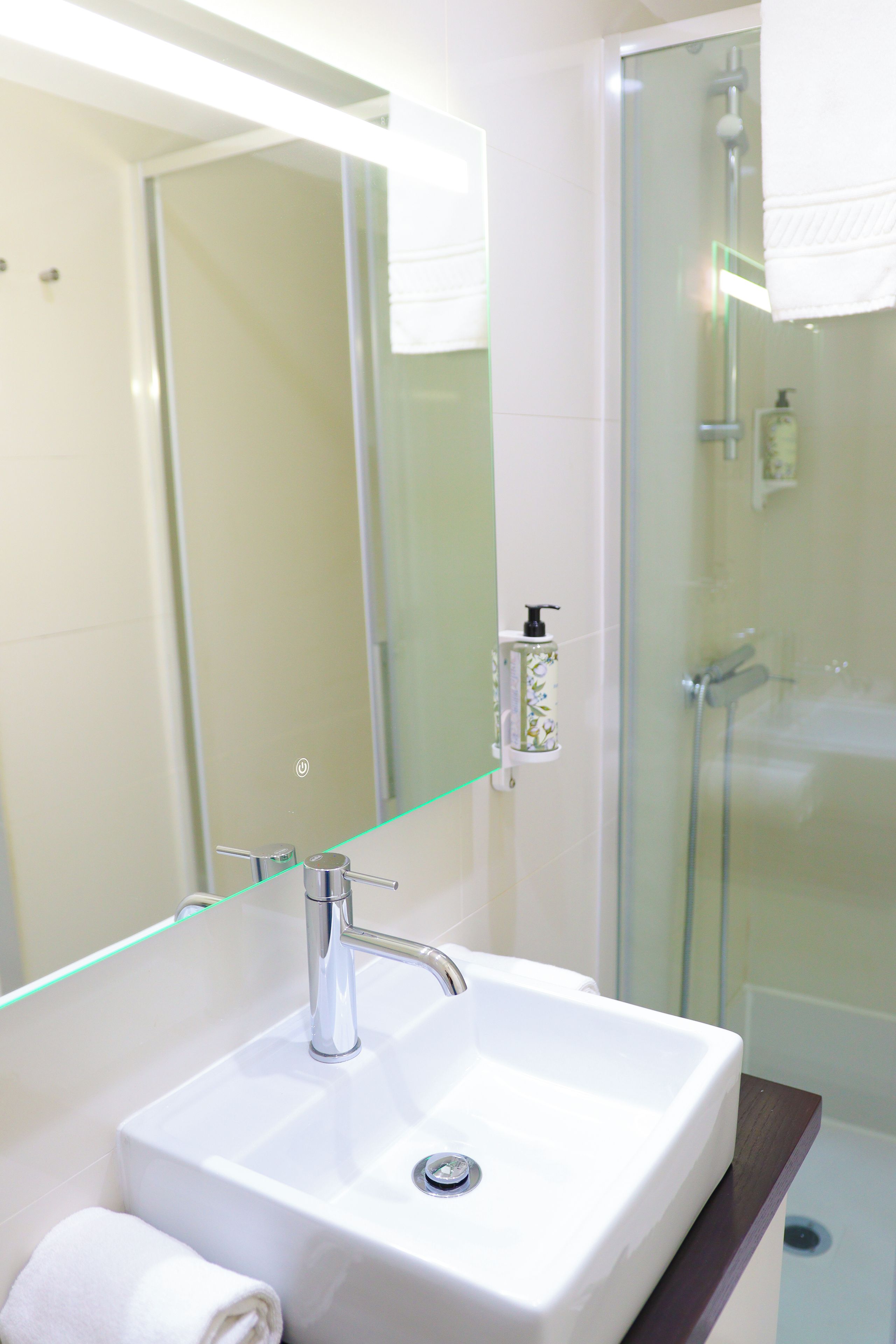 Une salle de bain avec un lavabo blanc, une douche en verre et un miroir avec un éclairage au-dessus.