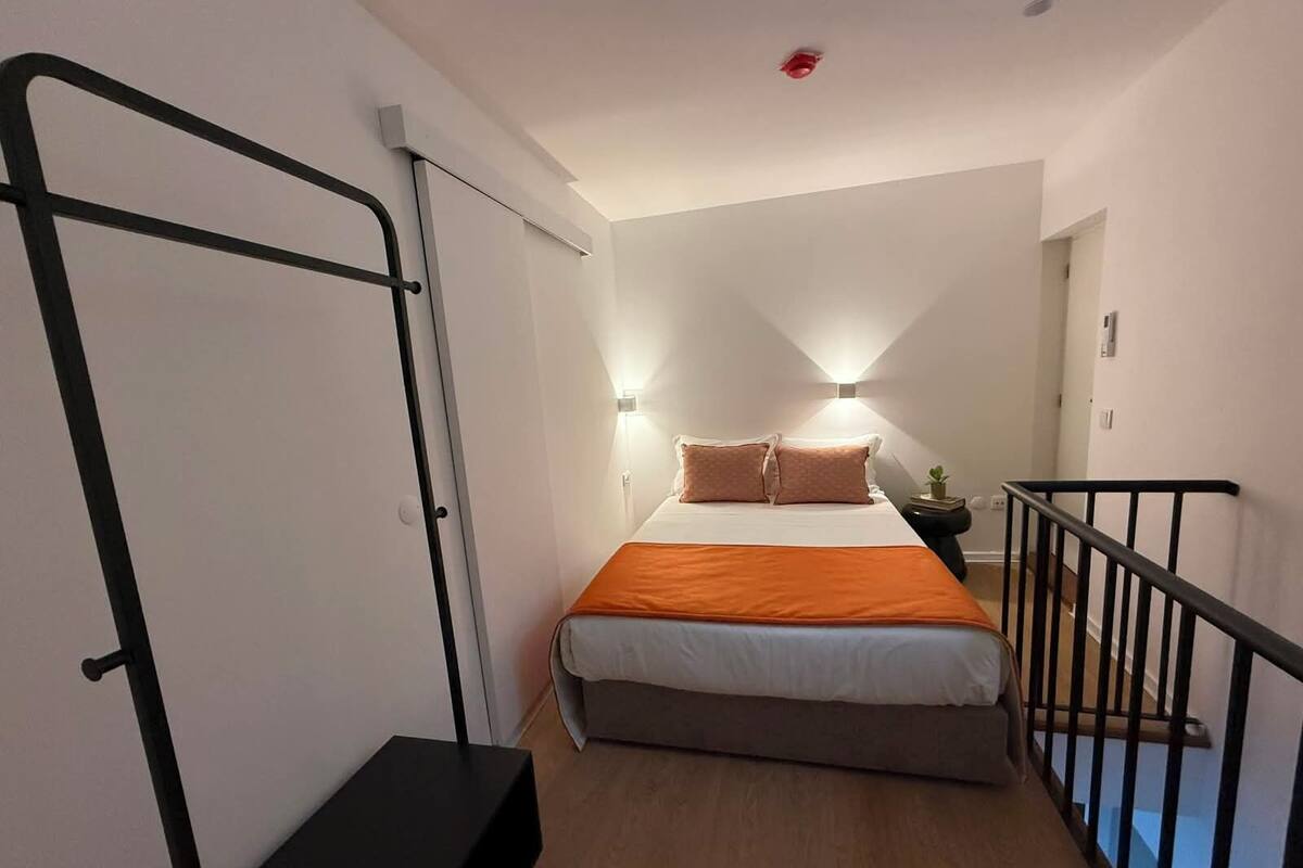 A bedroom with a bed, a bedside table, a small plant, and a black bench.