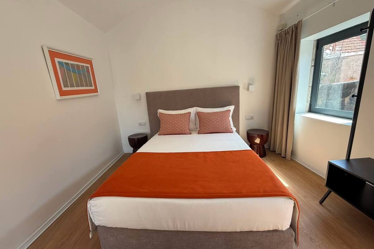 A hotel room with a large bed, two bedside tables, a window with curtains, and a framed picture on the wall.