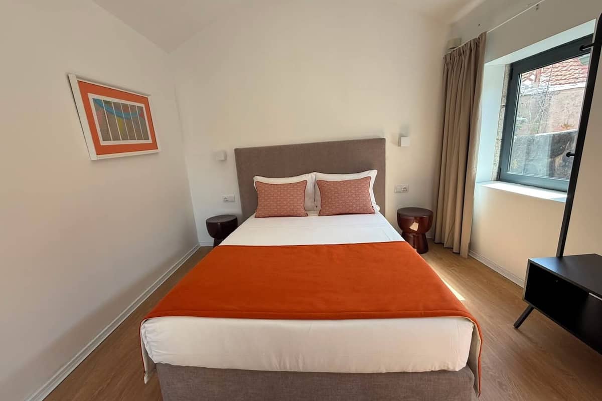 Habitación de hotel con una cama grande, dos mesitas de noche, una ventana con cortinas y un cuadro en la pared.