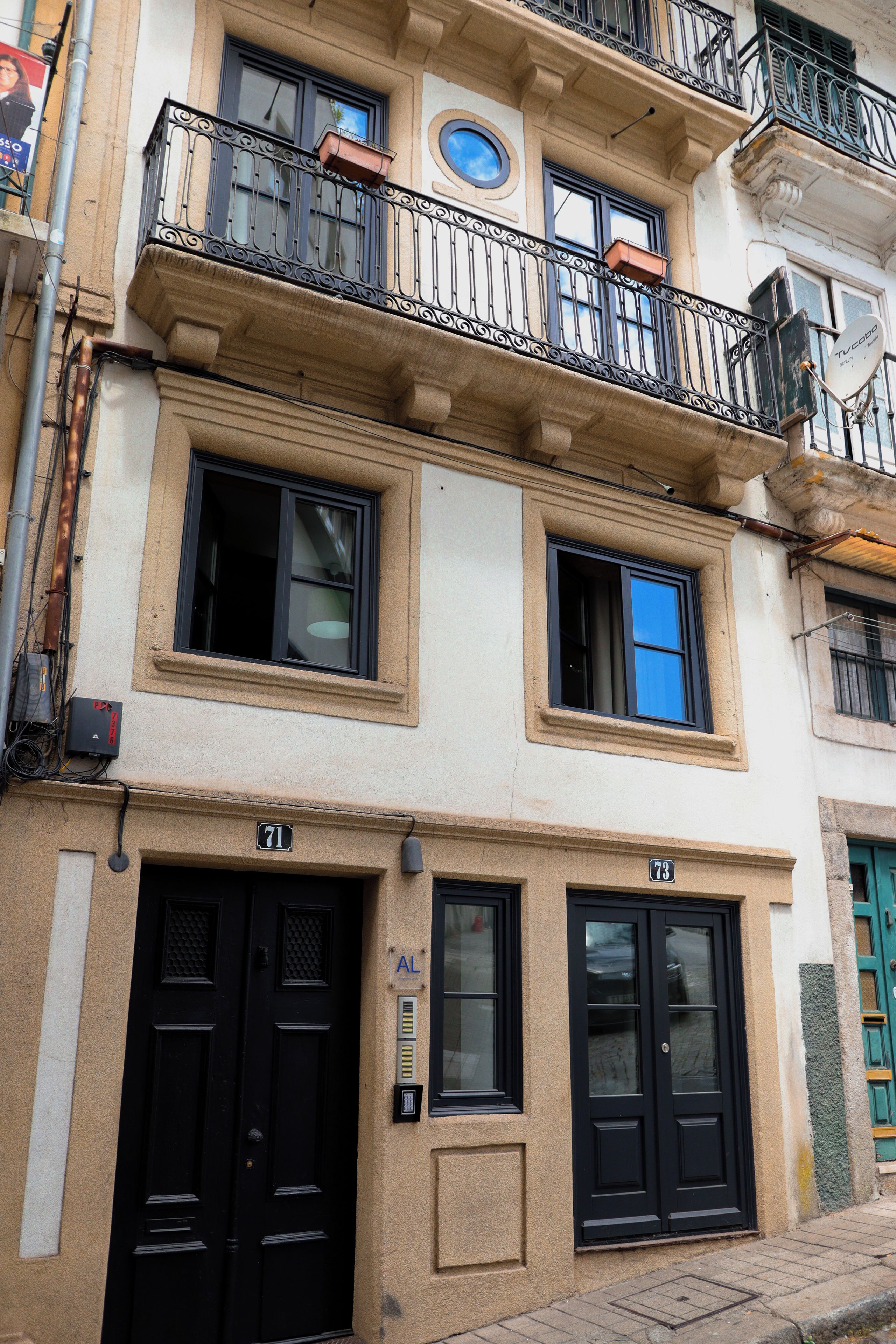 A multi-story building with a balcony, black doors, and a visible window.