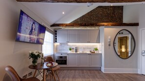 A modern kitchen with white cabinets, a dining area with a table and chairs, a large flat-screen TV, and a brick ceiling. - Marylebone Studios by DMONTRIO (London)