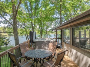 Una terraza con jacuzzi, asientos al aire libre y vistas a un lago.
