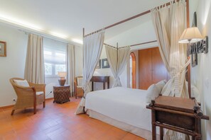 Ein Himmelsbett mit Vorhängen, ein Korbstuhl, ein Nachttisch und eine Lampe.