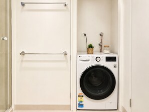 Une petite buanderie comprenant un lave-linge à chargement frontal, un porte-serviettes et une petite plante en pot.