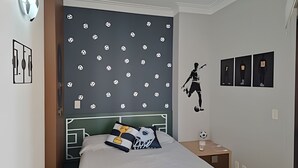 A bedroom with a bed, a nightstand, a wall with a soccer-themed design, and a door. - SHB - Futebol e Praia Beira Mar (Santos)