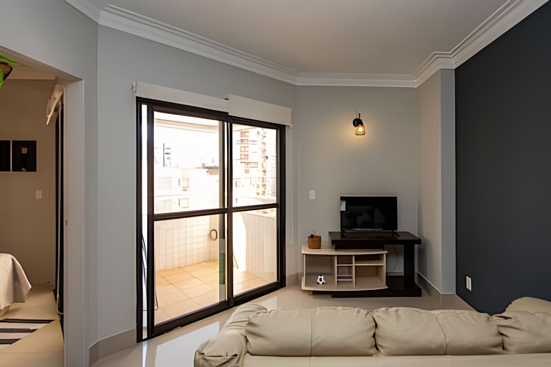 Sala de estar com sofá, televisão em móvel e grande janela com vista para edifícios.