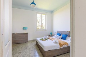 Une chambre à coucher avec un lit, une commode, une fenêtre et un luminaire suspendu.