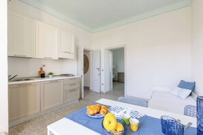 Une cuisine compacte avec des meubles blancs, un évier et un coin repas où une table est dressée pour le petit-déjeuner.