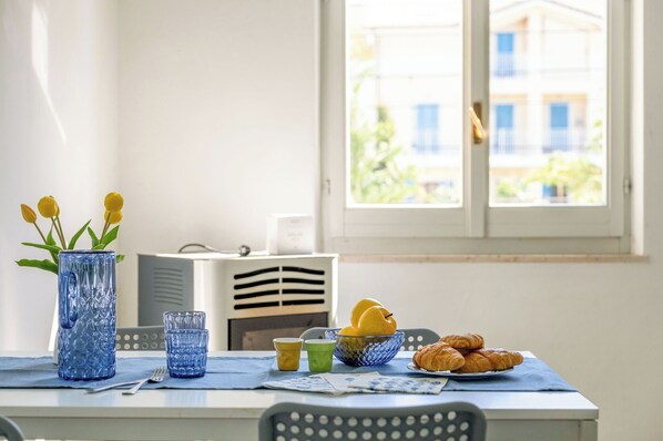 Une table à manger ornée d’un vase de tulipes jaunes, d’un saladier de poires, d’une assiette de croissants et, au fond, d’un four à micro-ondes.
