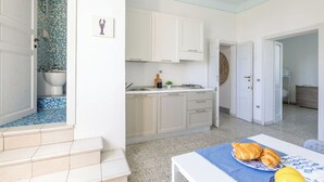 Ett kök med vita skåp, en diskho och en spis. Där finns ett matbord med en tallrik full av croissanter och en gul citron.