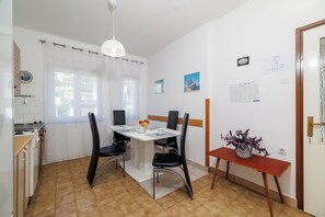 Ein Essbereich mit einem weißen Tisch, schwarzen Stühlen, einem kleinen Beistelltisch mit einer Vase und einem Fenster mit Vorhängen.