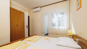 Hotellihuone, jossa on sänky, pyyhkeet, yöpöytälamppu, ilmastointilaite, ikkuna, jossa on verhot, ja ovi.