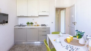 Een moderne keuken met witte kastjes, een inbouwoven en een eethoek met een tafel gedekt voor twee personen.