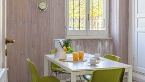 Spiseplads med et hvidt bord, grønne stole, et vindue med udsigt og et vægur.